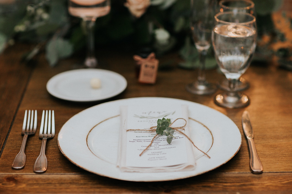 reception 10 X3 Place setting with a white plate, menu, and sprig tied with twine, surrounded by cutlery, a water glass, wine glass, and a butter plate with a single pat of butter.