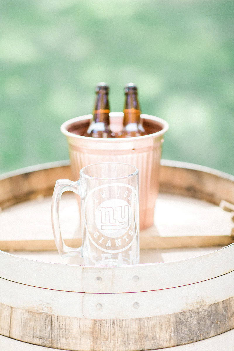 AllysonandSean335 X3 A clear glass NY Giants beer mug sits on a wooden barrel in front of a pink bucket holding three brown beer bottles.