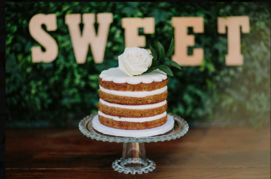 A three-layer naked cake with white icing and a white rose on top sits on a glass cake stand. The word "SWEET" is displayed in large letters in the background.